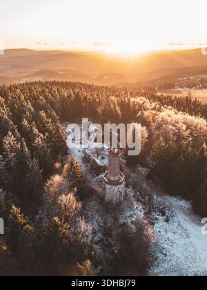 Der Aussichtsturm Stepanka steht im Winter im Isergebirge hoch. Die Sonne geht hinter den Hügeln unter und wirft Licht über verschneite Bäume. Die Gegend fühlt sich ruhig und ruhig an. Stockfoto