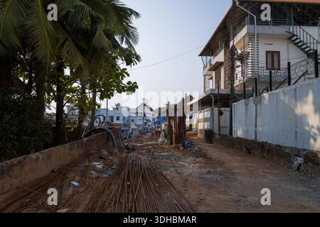 Fort Kochi, Indien - 16. März 2023: Eine unbefestigte Straße in Fort Kochi wird im Bau gehalten, an der entlang der Straße mehrere Metallstangen, Bauschutt, Palmen und mehrstöckige Wohngebäude zu sehen sind. Stockfoto