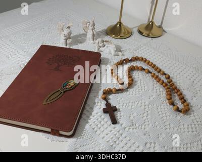 Katholische Ecke zu Hause. Engelsfigur, Rosenkranzperlen aus Holz, Kreuz und Gebetsbuch. Glaube, Symbole und Traditionen. Stockfoto