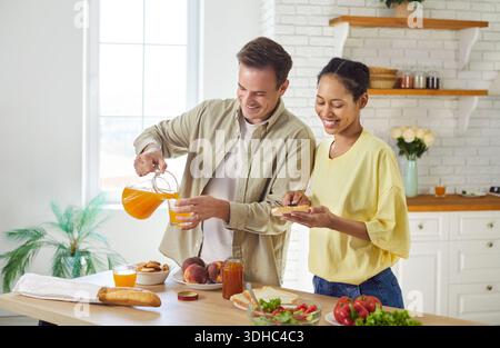 Paare, die zusammen Frühstück in der Küche kochen, Mann, der Saft ins Glas gießt Stockfoto