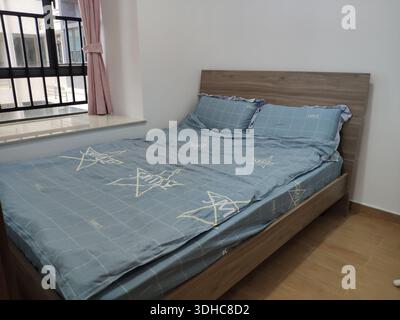 Modernes Holzbett mit blauem Sternmuster in einem minimalistischen Schlafzimmer Stockfoto