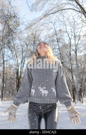 Ziemlich glückliches Mädchen in einem warmen grauen Hut und Pullover. Strickpullover mit Elchmuster. Hände in warmen Fäustlingen. Authentische ukrainische handgefertigte Kleidung. Stockfoto