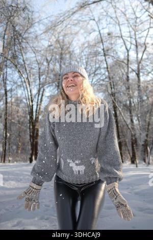 Ziemlich glückliches Mädchen in einem warmen grauen Hut und Pullover. Strickpullover mit Elchmuster. Hände in warmen Fäustlingen. Authentische ukrainische handgefertigte Kleidung. Stockfoto