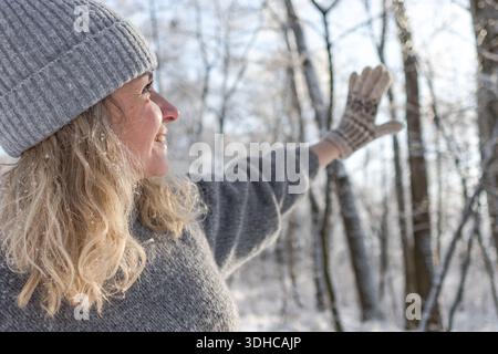 Ziemlich glückliches Mädchen in einem warmen grauen Hut und Pullover. Strickpullover mit Elchmuster. Hände in warmen Fäustlingen. Authentische ukrainische handgefertigte Kleidung. Stockfoto