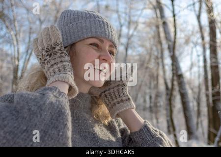 Ziemlich glückliches Mädchen in einem warmen grauen Hut und Pullover. Strickpullover mit Elchmuster. Hände in warmen Fäustlingen. Authentische ukrainische handgefertigte Kleidung. Stockfoto