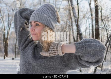 Ziemlich glückliches Mädchen in einem warmen grauen Hut und Pullover. Strickpullover mit Elchmuster. Hände in warmen Fäustlingen. Authentische ukrainische handgefertigte Kleidung. Stockfoto