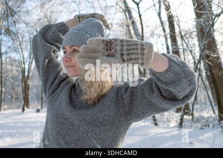 Ziemlich glückliches Mädchen in einem warmen grauen Hut und Pullover. Strickpullover mit Elchmuster. Hände in warmen Fäustlingen. Authentische ukrainische handgefertigte Kleidung. Stockfoto