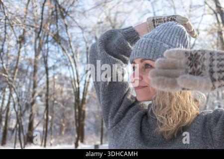 Ziemlich glückliches Mädchen in einem warmen grauen Hut und Pullover. Strickpullover mit Elchmuster. Hände in warmen Fäustlingen. Authentische ukrainische handgefertigte Kleidung. Stockfoto