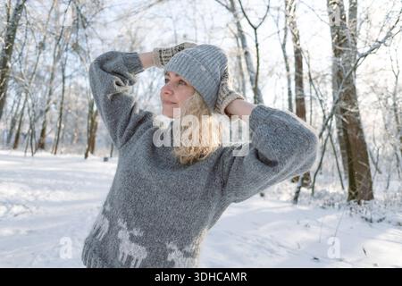 Ziemlich glückliches Mädchen in einem warmen grauen Hut und Pullover. Strickpullover mit Elchmuster. Hände in warmen Fäustlingen. Authentische ukrainische handgefertigte Kleidung. Stockfoto