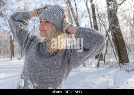 Ziemlich glückliches Mädchen in einem warmen grauen Hut und Pullover. Strickpullover mit Elchmuster. Hände in warmen Fäustlingen. Authentische ukrainische handgefertigte Kleidung. Stockfoto
