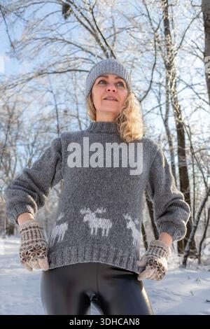 Ziemlich glückliches Mädchen in einem warmen grauen Hut und Pullover. Strickpullover mit Elchmuster. Hände in warmen Fäustlingen. Authentische ukrainische handgefertigte Kleidung. Stockfoto