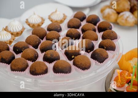 Schokoladentrüffel in rosa Kapseln und Tartlets mit Proteincreme. Portionierte Schokoladenbonbons, bestreut mit Kakao und Tartlets mit Meringue in A Stockfoto