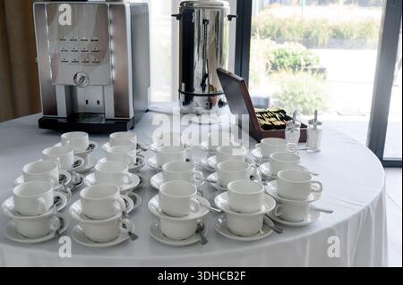 Kaffeestation mit professioneller Kaffeemaschine und weißen Tassen auf einem Tisch für geschäftliche Veranstaltungen. Selbstbedienungstisch mit Kaffeemaschine und Stockfoto