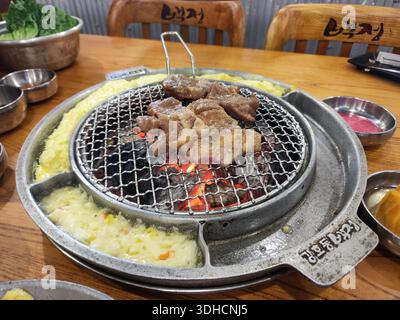 Koreanisches BBQ-Menü mit brausendem Fleisch auf Holzkohlegrill, serviert mit Reis und Beilagen Stockfoto