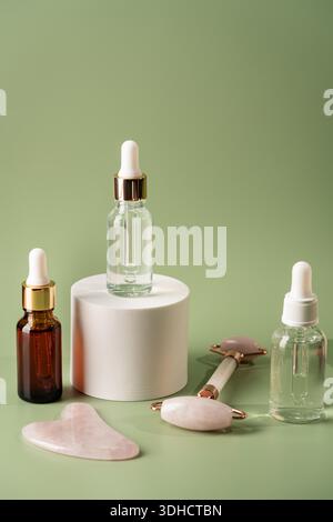 Jade-Gesichtsrollen und Gua-Sha-Steine für Beauty-Gesichtsmassage-Therapie, Artikel für die häusliche Behandlung mit Skin Care Anti-Aging-Tools und Gesichtsserum auf grünem Hintergrund Stockfoto