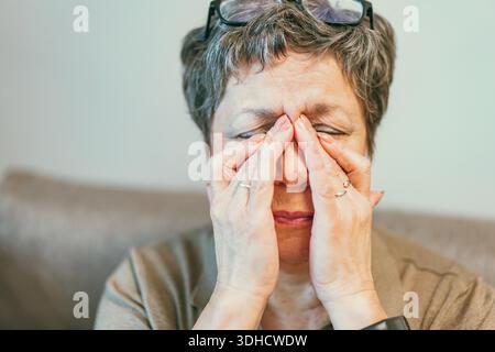 Nahaufnahme der Seniorin fühlen sich ungesund Touch Massage Augen mit starken Migräne-Symptomen oder Kopfschmerzen, ältere Frau nehmen Brille, die unter Schwindel leidet || Modell veröffentlicht Stockfoto