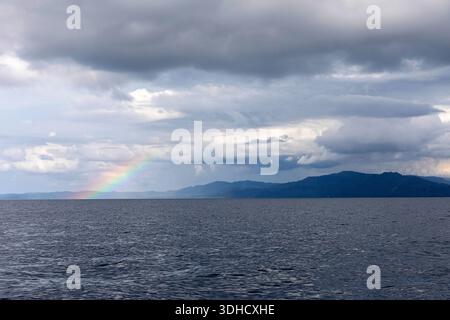 Regenbogen über dem Meer und bergigem Land in der Nähe von bunaken im Norden von sulawesi in indonesien, stürmische Wolken Stockfoto