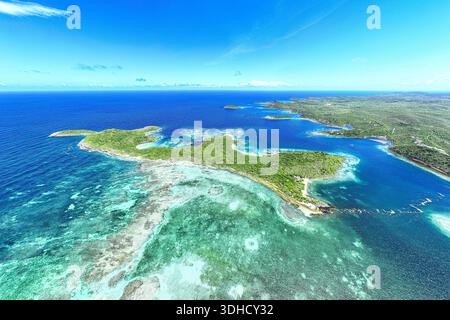 Aus der Vogelperspektive auf das pulsierende türkisfarbene Wasser, das die üppigen, grünen Inseln unter einem klaren blauen Himmel umgibt, Antigua, Antigua und Barbuda. Stockfoto