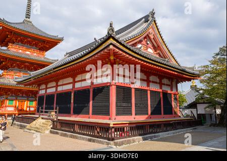 Kyoto, Japan - 16. Oktober 2023: Die Sutra-Halle und ein Teil der dreistöckigen Sanjunoto-Pagode im Kiyomizu-dera-Tempel sind mit traditioneller Holzarchitektur und lebhaften Rot- und Weißtönen unter einem teilweise bewölkten Himmel zu sehen. Stockfoto