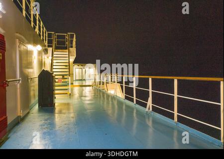 Unbekannter Ort - 13. September 2023: Das Bild zeigt das Außendeck einer Fähre bei Nacht mit einer Treppe, beleuchtetem Durchgang, Geländer und einem Mülleimer unter künstlicher Beleuchtung. Stockfoto