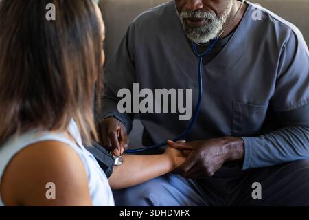 Afroamerikanischer männlicher Anbieter bei grauen Peelings, der Patienten in der Klinik mit Stethoskop und Manschette untersucht Stockfoto