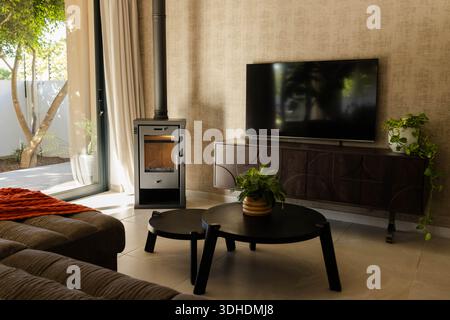 Ein schwarzer Holzofen sitzt neben der Glasschiebetür und wirft sanfte Schatten auf die Fliesen Stockfoto