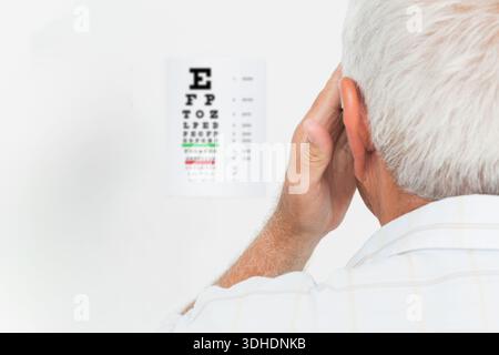Snellen-Augendiagramm mit grünen und roten Linien, während die Hand während des Tests ein Auge bedeckt. Sehschärfe, Augenheilkunde, Augenheilkunde, Augenoptometrie, Senior, Patient Stockfoto