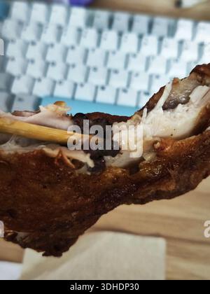 Nahaufnahme einer Hand, die einen knusprigen, frittierten Hühnerflügel mit Stäbchen über einem Tastaturhintergrund hält Stockfoto