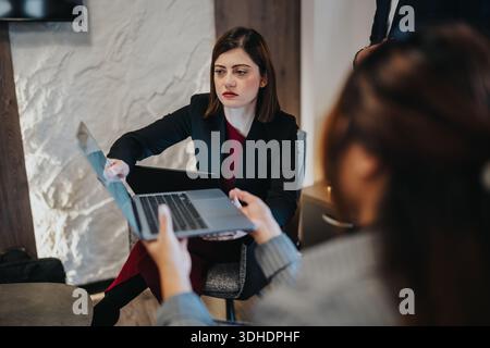 Geschäftsfrau präsentiert sich auf Laptop und Dokument während einer Bürositzung in einem modernen Arbeitsbereich Stockfoto
