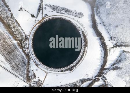 Von oben nach unten auf einen perfekt runden Teich in einem verschneiten Feld Stockfoto