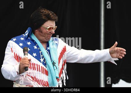 Elvis-Imitator im Kostüm der amerikanischen Flagge tritt auf der Bühne mit Mikrofon auf Stockfoto