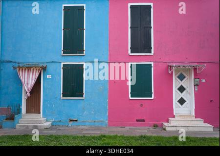 Vorderansicht von zwei traditionellen farbenfrohen Häusern auf der Insel Burano, Venedig, Italien. Die leuchtenden blauen und rosa Fassaden mit grünen Holzläden Stockfoto