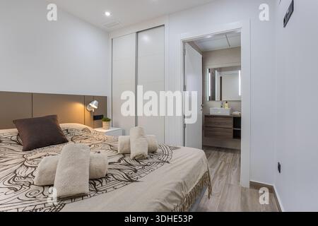 Einladendes Schlafzimmer mit neutraler Einrichtung, Holzfußboden und eigenem Bad mit Kosmetikbereich. Stockfoto