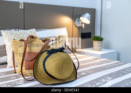 Komfortables, modernes Schlafzimmer mit Reiseaccessoires, gestreifter Bettwäsche und warmer Beleuchtung. Stockfoto