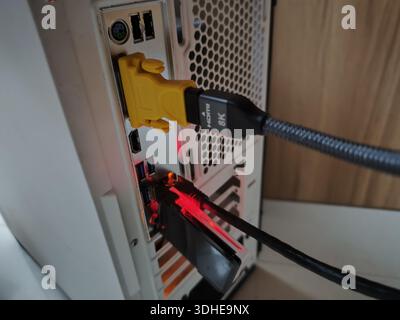 Nahaufnahme von HDMI- und USB-Kabeln, die an einen Computerturm mit roter LED-Beleuchtung angeschlossen sind Stockfoto