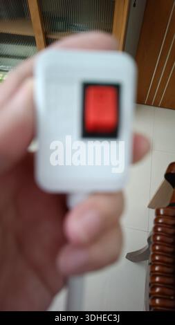 Hand hält einen weißen elektrischen Stecker mit rotem Schalter Stockfoto