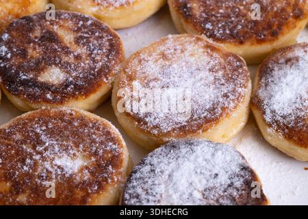 Goldener gebratener Syrniki mit Zucker bestreut, Nahaufnahme von warmen Hüttenkäse-Pfannkuchen mit knusprigen Kanten und weichen Zentren, rustikales Pergament, Morgenlicht Stockfoto
