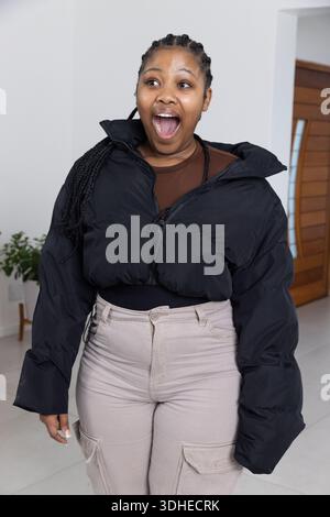 Afroamerikanerin, die mit offenem Mund und weit im Eingangsbereich steht und eine Pufferjacke trägt Stockfoto