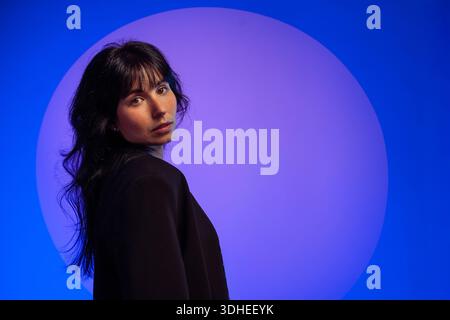 Junge Frau, die mit Neon-Ambient-Beleuchtung zurückblickt Stockfoto