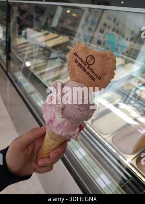 Halten Sie eine Erdbeereiskegel mit herzförmiger Waffel vor einer Eisvitrine Stockfoto