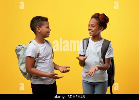 Glückliche afroamerikanische Schüler, die sich auf Gelb unterhalten Stockfoto