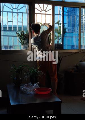 Eine Person, die ein großes Fenster in einem schwach beleuchteten Raum mit Stadtgebäuden putzt Stockfoto