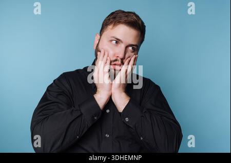 Mann in schwarzem Hemd, der nachdenklich vor blauem Hintergrund aussieht Stockfoto