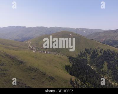 Aus der Vogelperspektive eines Bergdorfes in Georgien mit Vorgebirgen des Kaukasus, spärlichem Schnee, Häusern, Bauernhöfen, einem Kuppelgipfel, und einen Nadelwald Stockfoto