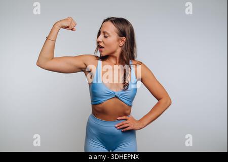 Frau in blauer Sportbekleidung, die ihre Armmuskeln selbstbewusst anspannt. Stockfoto