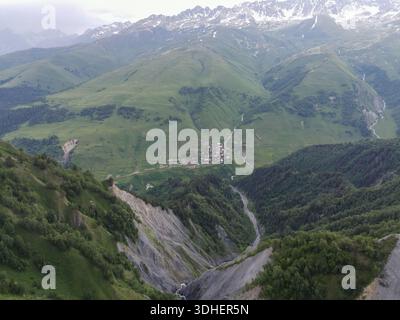 Aus der Vogelperspektive zeigt ein Dorf Svaneti in Georgia an einem sich windenden Fluss unter den Gipfeln des Großen Kaukasus, mit bewaldeten Hängen, grauem Felsen, Weiden usw. Stockfoto