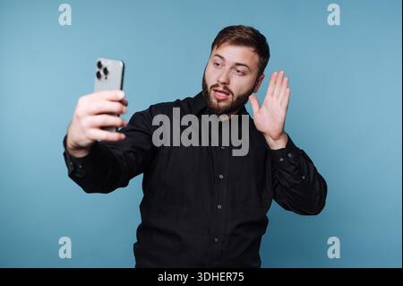 Mann in schwarzem Hemd, der ein Selfie mit überraschtem Ausdruck macht. Stockfoto