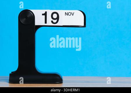 Moderner Flipkalender mit dem 19. November auf einem Holztisch mit hellblauem Hintergrund Stockfoto