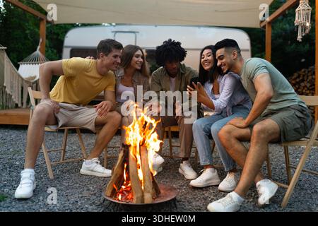 Eine Gruppe von fröhlichen, vielfältigen Freunden, die Zeit in der Nähe des Lagerfeuers verbringen, Campingurlaub mit Wohnmobil verbringen, Spaß im Freien haben Stockfoto