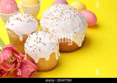 Köstliche Osterkuchen, Eier und Tulpen auf gelbem Hintergrund, Nahaufnahme Stockfoto